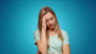 Mavi arka planda duran genç bir kadının başı ağrıyor.