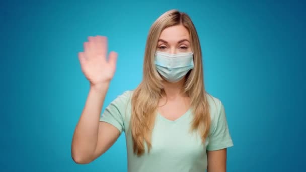 Lycklig kvinna i medicinsk mask skakar hennes hand, hälsning någon, blå bakgrund — Stockvideo