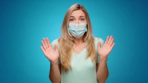Женщина в медицинской маске на лице очень счастлива и хлопает в ладоши на синем фоне — стоковое видео