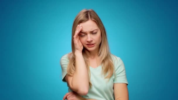 Młoda kobieta ma ból głowy stojący na niebieskim tle — Wideo stockowe