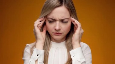 Mavi arka planda duran genç bir kadının başı ağrıyor.