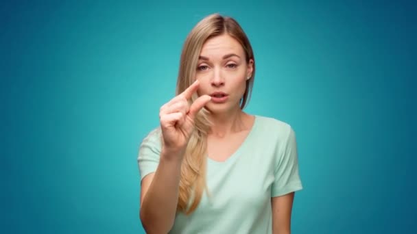 Besviken ung kvinna visar liten storlek gest mot blå bakgrund — Stockvideo
