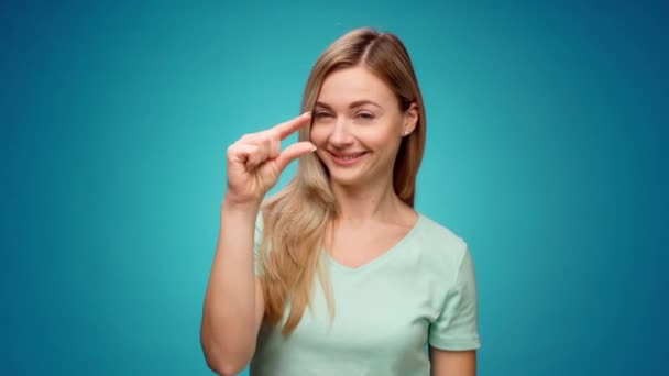 Mujer joven decepcionada mostrando gesto de pequeño tamaño sobre fondo azul — Vídeos de Stock