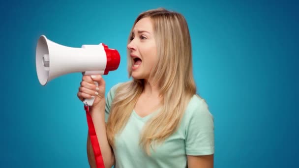 Mujer joven rubia anunciando algo usando altavoz sobre fondo azul — Vídeos de Stock