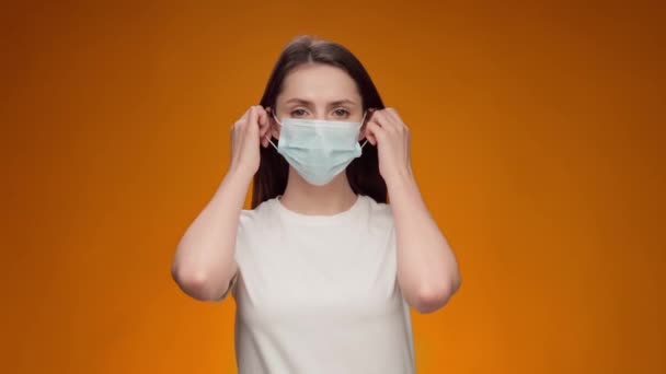 Jovem tira máscara médica e sorri contra fundo amarelo — Vídeo de Stock