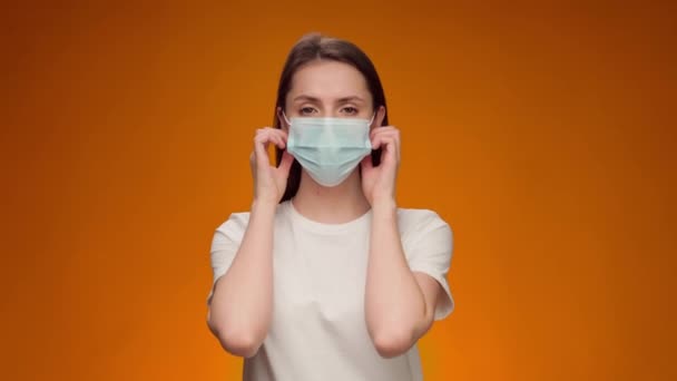 Νεαρή γυναίκα βγάζει την ιατρική μάσκα και χαμογελά σε κίτρινο φόντο — Αρχείο Βίντεο