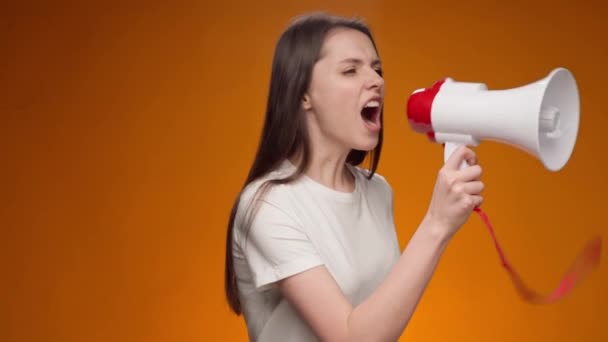 Young woman announcing something using loudspeaker against yellow background — Stock Video