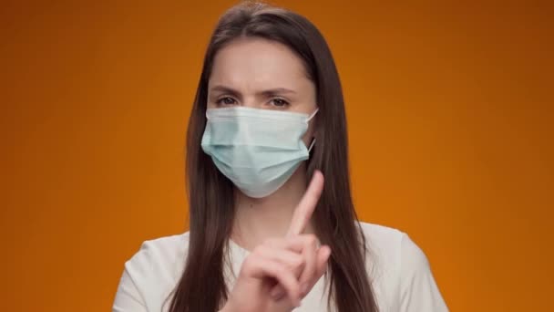 Frumoasa femeie în mască medicală dezaprobă gestul cu degetul pe fundal galben — Videoclip de stoc