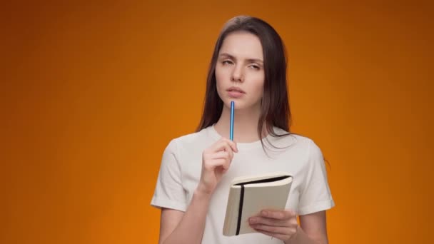 Nachdenkliche junge Frau macht sich Notizen im Notizblock vor gelbem Hintergrund — Stockvideo