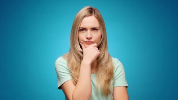 Thoughtful woman looking aside with pensive expression againast blue background — Stock Video