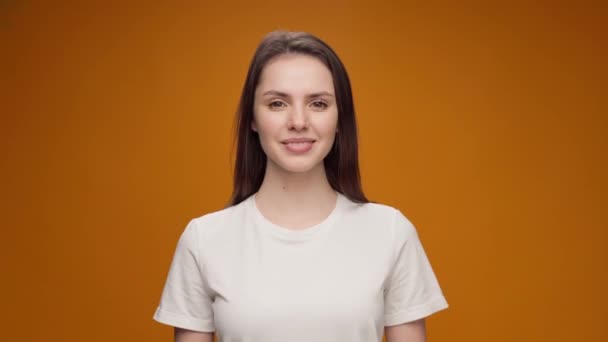 Aantrekkelijke jonge vrouw staande tegen gele achtergrond en glimlachend, kijkend naar camera — Stockvideo