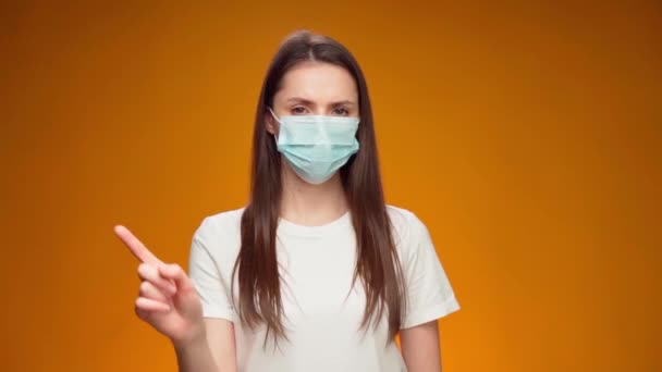 Mujer bonita con máscara médica hace gesto de desaprobación con el dedo contra el fondo azul — Vídeo de stock