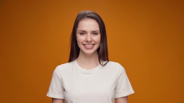 Attraktiv ung kvinna står mot gul bakgrund och ler, tittar på kameran — Stockvideo