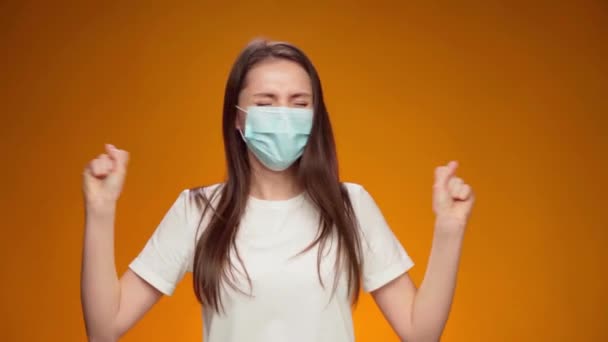 Frau mit medizinischer Maske im Gesicht ist sehr glücklich und klatscht in die Hände vor gelbem Hintergrund — Stockvideo