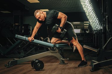 Kaslı genç adam karanlık bir spor salonunda ağırlık kaldırıyor.