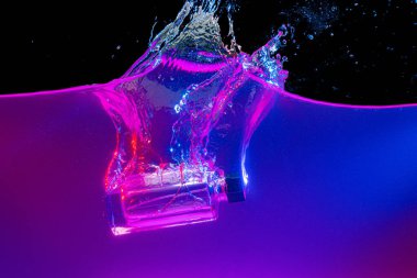 Parfüm şişesi neon ışıkta suya dalıyor.