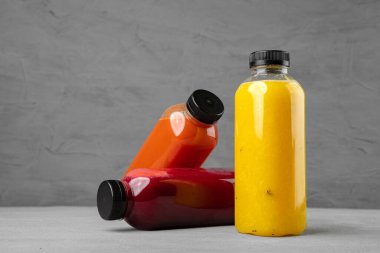 Gri arka planda taze sıkılmış meyve suyu olan üç plastik şişe.