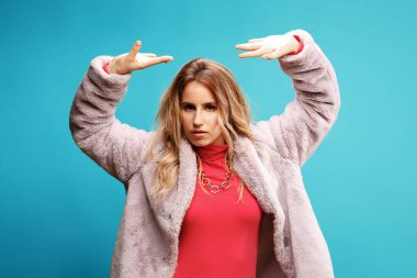 Pembe ceketli zarif genç bayan dansçı mavi arka planda poz veriyor.