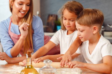 Çocuklarıyla mutfakta hamur yoğuran bir kadın.