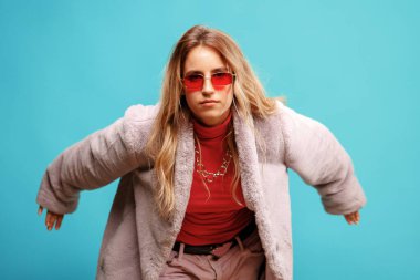 Pembe ceketli zarif genç bayan dansçı mavi arka planda poz veriyor.