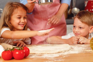 Çocuklarıyla mutfakta hamur yoğuran bir kadın.