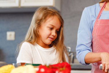 Gülümseyen küçük kız mutfakta annesine yardım ediyor.