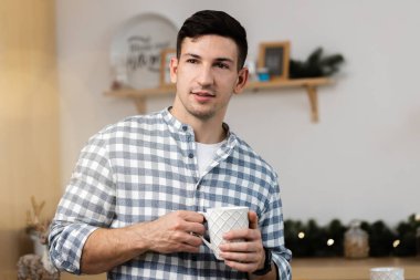 Genç adam mutfakta sıcak içecek içiyor.