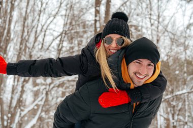 Mutlu çift dışarıda karlı parkta sarılıp gülümsüyor.
