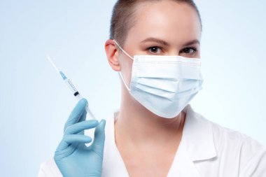 Maskeli kısa saçlı kadın doktor elinde şırıngayla ilaç taşıyor.