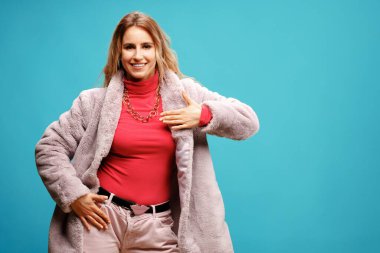 Pembe ceketli zarif genç bayan dansçı mavi arka planda poz veriyor.