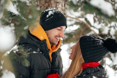 Mutlu çift dışarıda karlı parkta sarılıp gülümsüyor.