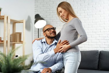 Engelli kocasının elini tutan hamile bir kadın tekerlekli sandalyede oturuyor.