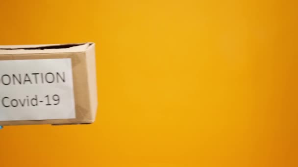 Mãos humanas segurando caixa de papelão com Coronavirus Doações contra fundo amarelo — Vídeo de Stock