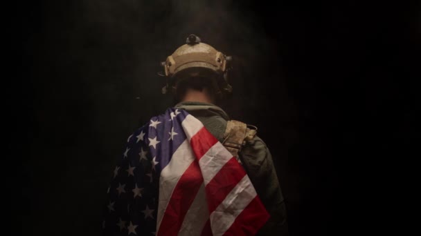 Special forces soldaat die met zijn rug naar ons toe staat in het donker en de Amerikaanse vlag vasthoudt — Stockvideo