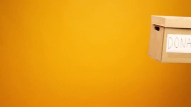Eldivenler içinde insan eli sarı arka planda diğerine bağış kutusunu uzatırken, Coronavirus bağışları yardımcı oluyor.