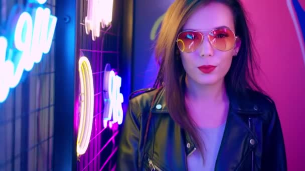 Femme mixte racée avec dreadlocks et lunettes posant près de mur de néon lumineux dans l'obscurité — Video