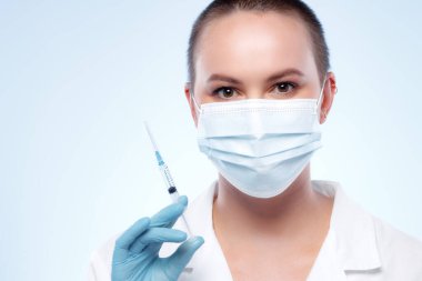 Maskeli kısa saçlı kadın doktor elinde şırıngayla ilaç taşıyor.