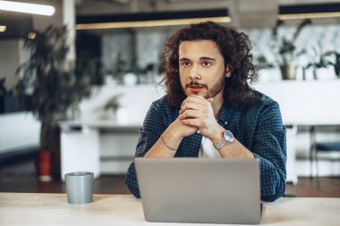 Genç işadamı çalışma masasında oturuyor ve bir şeyler düşünüyor.