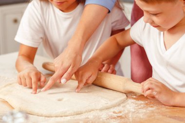 Çocuklarıyla mutfakta hamur yoğuran bir kadın.