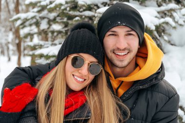 Mutlu çift dışarıda karlı parkta sarılıp gülümsüyor.