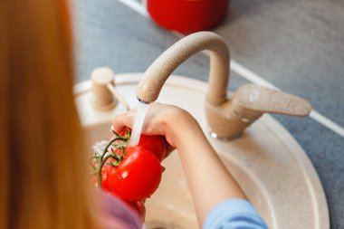 Tanınmayan bir kadın lavaboda taze domates yıkıyor.