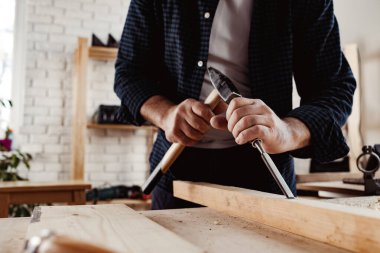 Bir marangozun elleri keski ve çekiçle çalışır.