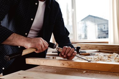 Bir marangozun elleri keski ve çekiçle çalışır.