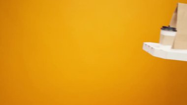 İnsanların elleri birbirlerinin yanından geçerken sarı stüdyo arka planında yiyecek paketleri taşıyorlar.