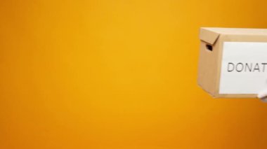 Eldivenler içinde insan eli sarı arka planda diğerine bağış kutusunu uzatırken, Coronavirus bağışları yardımcı oluyor.