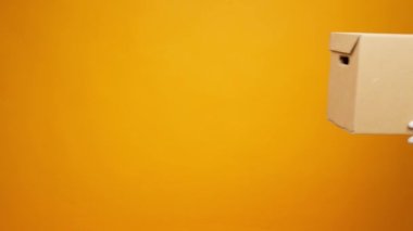 Eldivenler içinde insan eli sarı arka planda diğerine bağış kutusunu uzatırken, Coronavirus bağışları yardımcı oluyor.