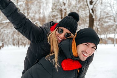 Mutlu çift dışarıda karlı parkta sarılıp gülümsüyor.