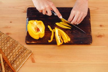 Kadın ahşap masada salata için sarı dolma biber kesiyor.