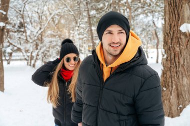 Mutlu çift dışarıda karlı parkta sarılıp gülümsüyor.