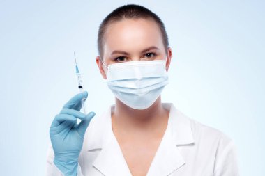 Maskeli kısa saçlı kadın doktor elinde şırıngayla ilaç taşıyor.